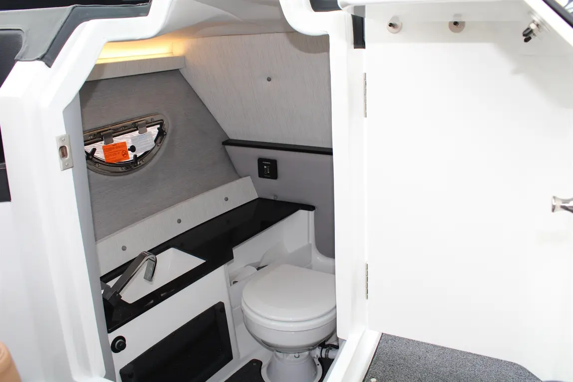 Interior view of a boat's bathroom featuring a toilet, sink, and a window, with modern gray and white decor.